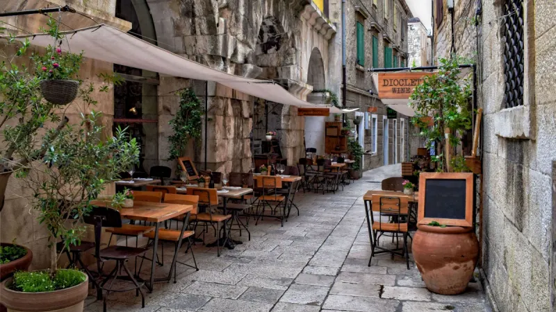 Gost rezervira stol u restoranu putem mobitela dok sjedi na terasi apartmana, simbolizirajući online rezervaciju u turističkoj destinaciji.
